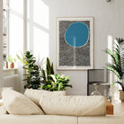 A large framed abstract blue and black print displayed in a modern white living room filled with plants, lending boldness and calm to the contemporary decor.