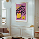 A framed art print featuring a colorful retro-style cocktail illustration with the text 'AMARETTO SOUR' on a pink background, displayed on a white wall in a modern, elegant room.