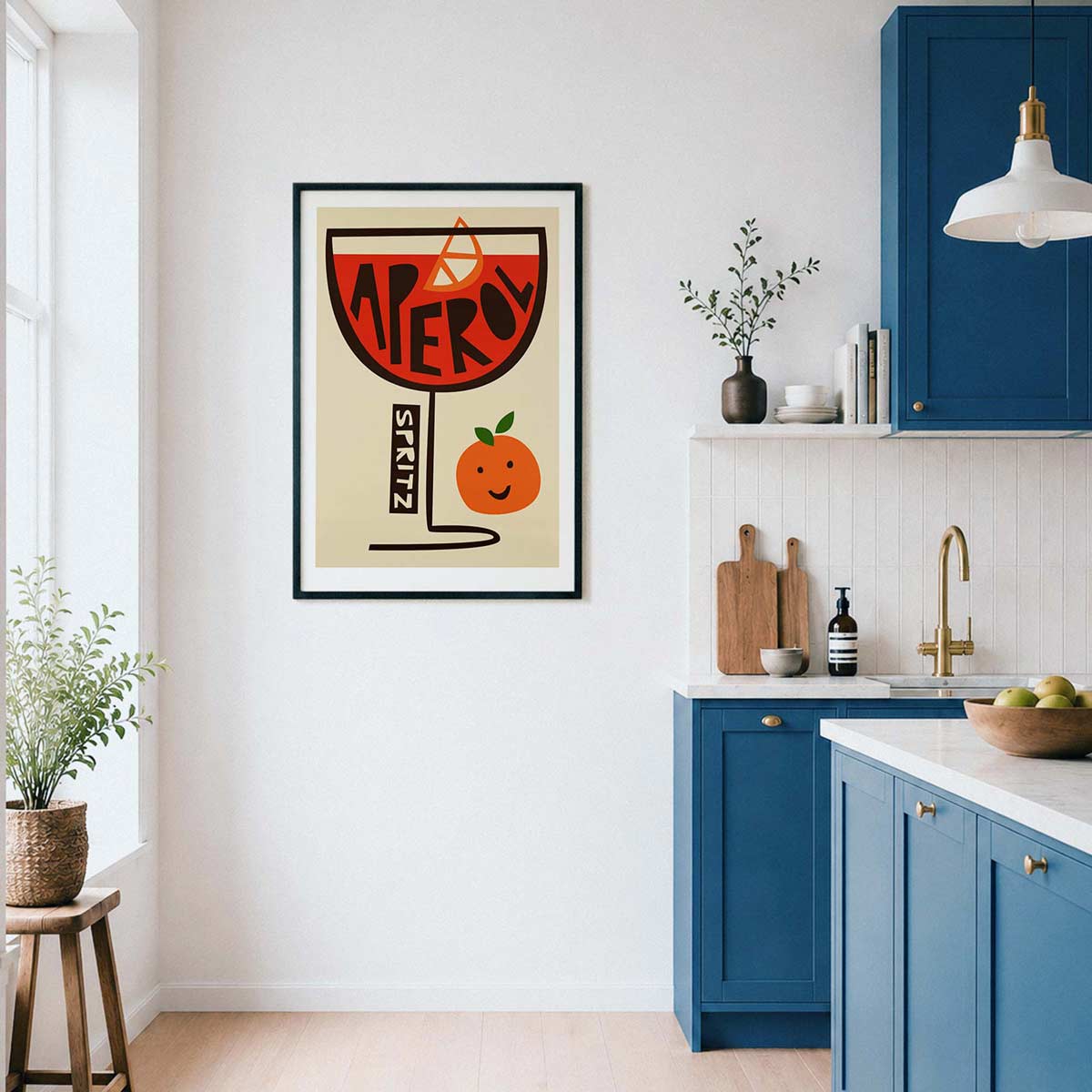 A framed art print featuring a retro cocktail glass with the word 'APEROL' and a smiling orange, displayed on a white wall in a modern kitchen with blue cabinets.