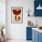 A framed art print featuring a retro cocktail glass with the word 'APEROL' and a smiling orange, displayed on a white wall in a modern kitchen with blue cabinets.