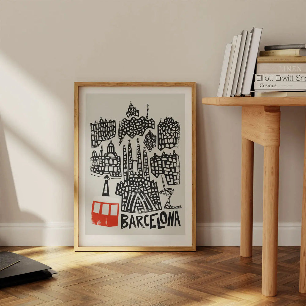 Framed Barcelona print leaning against a wall on a wooden floor, styled next to books and shelves, showcasing the print’s dynamic architectural shapes and playful composition.
