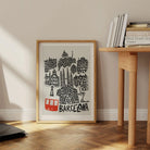 Framed Barcelona print leaning against a wall on a wooden floor, styled next to books and shelves, showcasing the print’s dynamic architectural shapes and playful composition.
