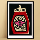 BBQ Sauce art print featuring a stylised red bottle with graphic face label and bold black background, framed on beige wall.