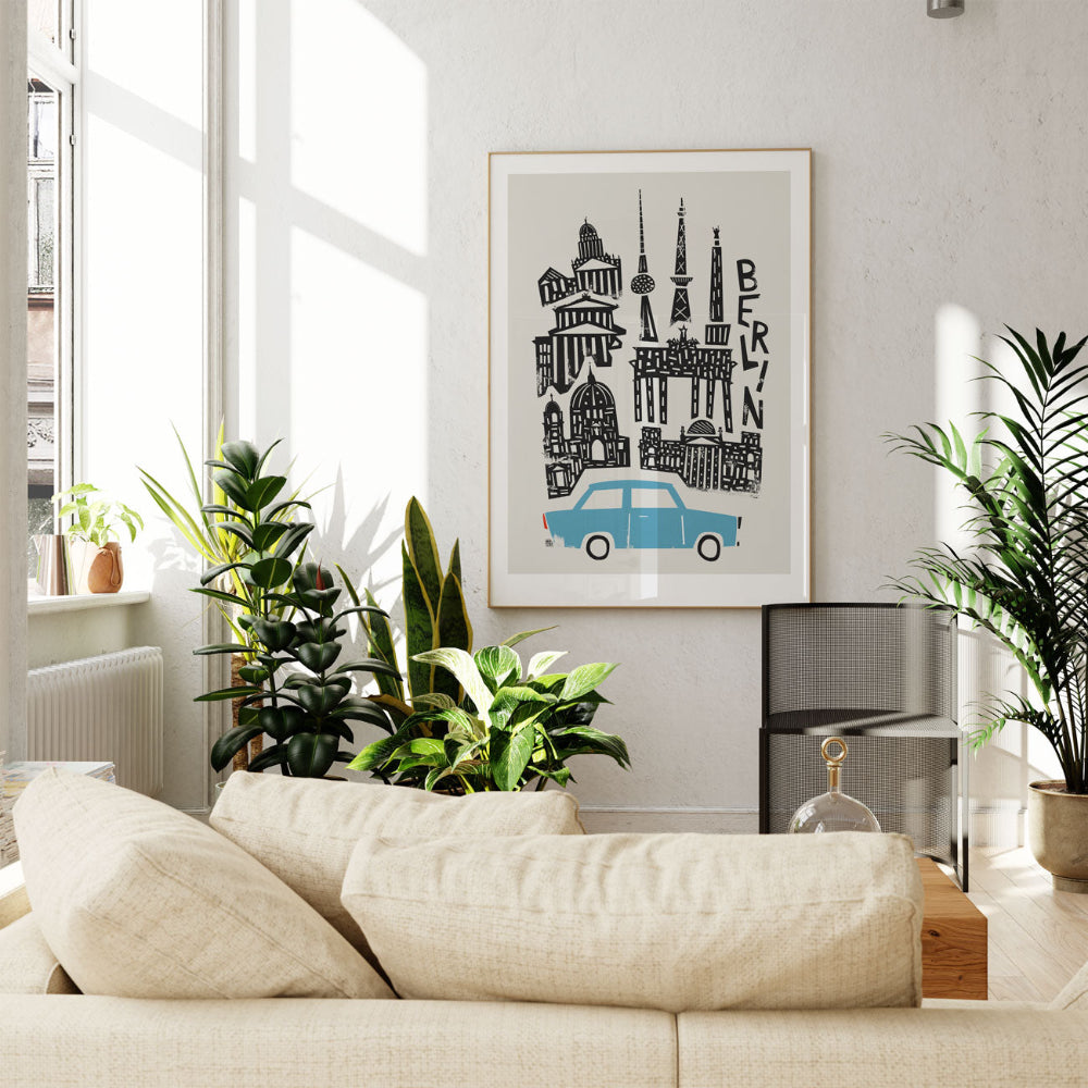 Framed Berlin cityscape artwork displayed above a neutral-toned sofa in a plant-filled living room, creating a modern, travel-inspired vibe.
