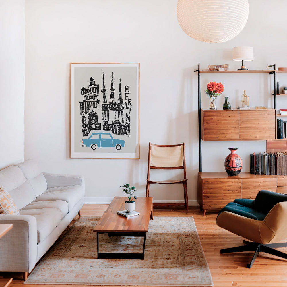 Berlin poster with a retro blue car grounding the scene, hanging in a mid-century modern interior with warm wood furniture and curated decor.
