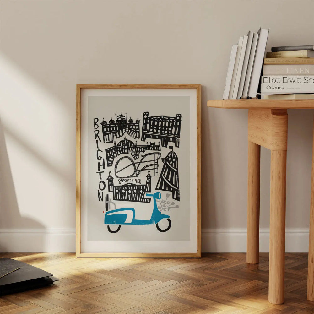 Framed Brighton city art print resting on a wooden floor beneath a desk, bringing a playful yet stylish coastal charm to the space.
