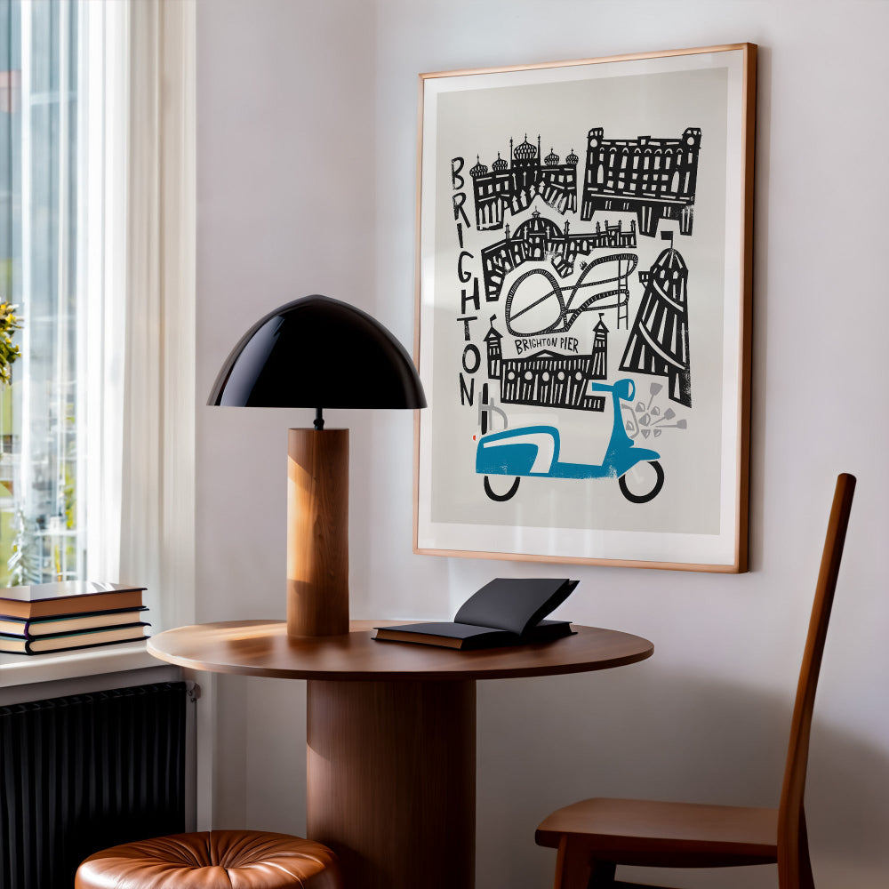 Brighton cityscape print hung above a desk nook with a black dome lamp, blending mid-century style with coastal flair in a relaxed home office setting.
