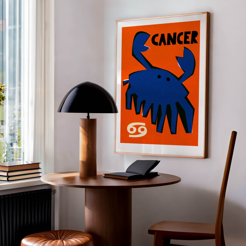 Cancer zodiac poster framed above a small table in a bright modern room with a lamp and warm wood tones.
