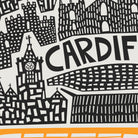 A close-up of a graphic print featuring black hand-drawn cityscape illustrations, including a clock tower and stylized buildings, with the word 'CARDIFF' in large black letters on a white background and a thin orange stripe at the bottom.