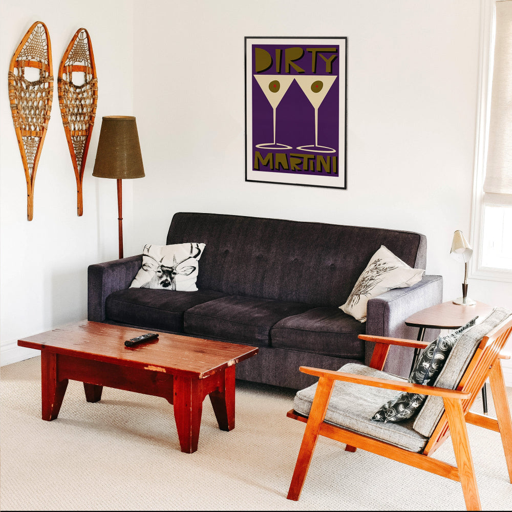 Dirty Martini print hanging above a dark sofa in a cosy retro living space with vintage skis and warm wood tones.
