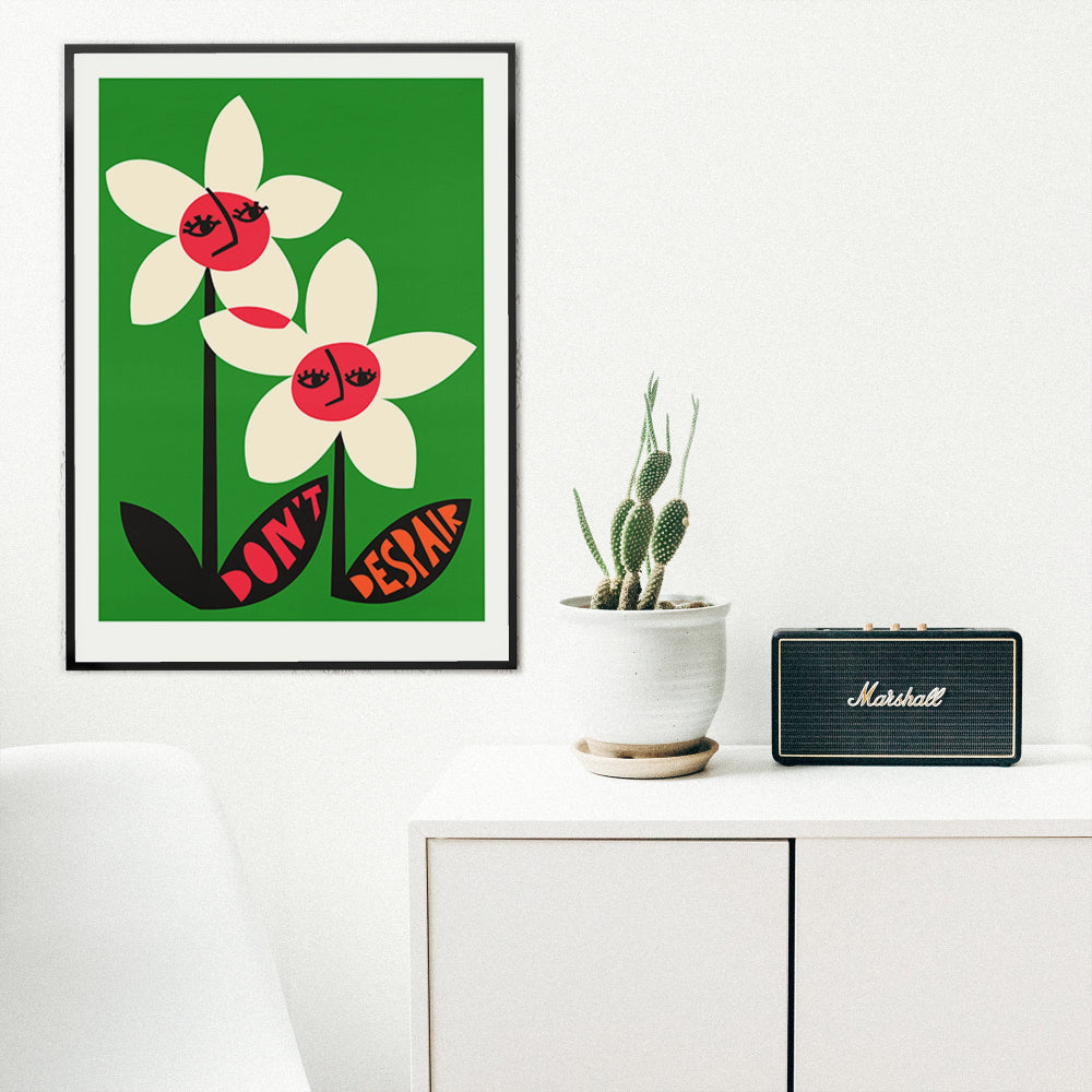 Don’t Despair flower artwork framed in a bright, white room beside a plant and cabinet speaker.