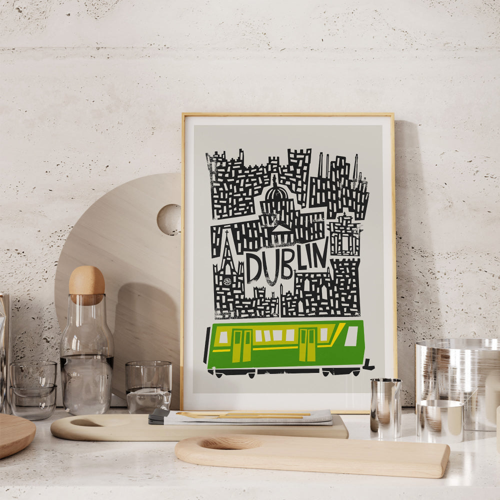Framed Dublin print styled on a soft-toned arched shelf with ceramics, showing the crisp contrast between monochrome line art and the punchy green tram illustration.