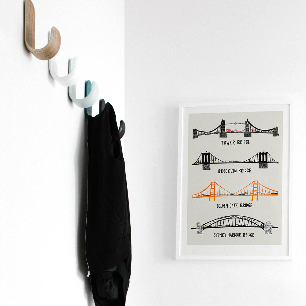 Famous bridges art print styled in a light hallway next to wall hooks and a black coat, adding character and travel nostalgia to a functional space.