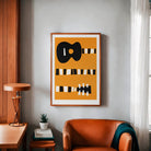 Guitar art print hanging above a rust-orange armchair and side table in a cosy living room