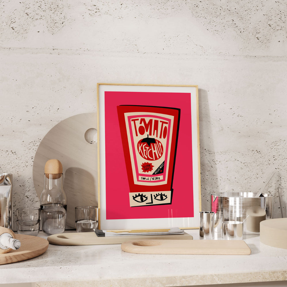 Ketchup bottle print framed on a kitchen shelf with stone backdrop and scattered barware.
