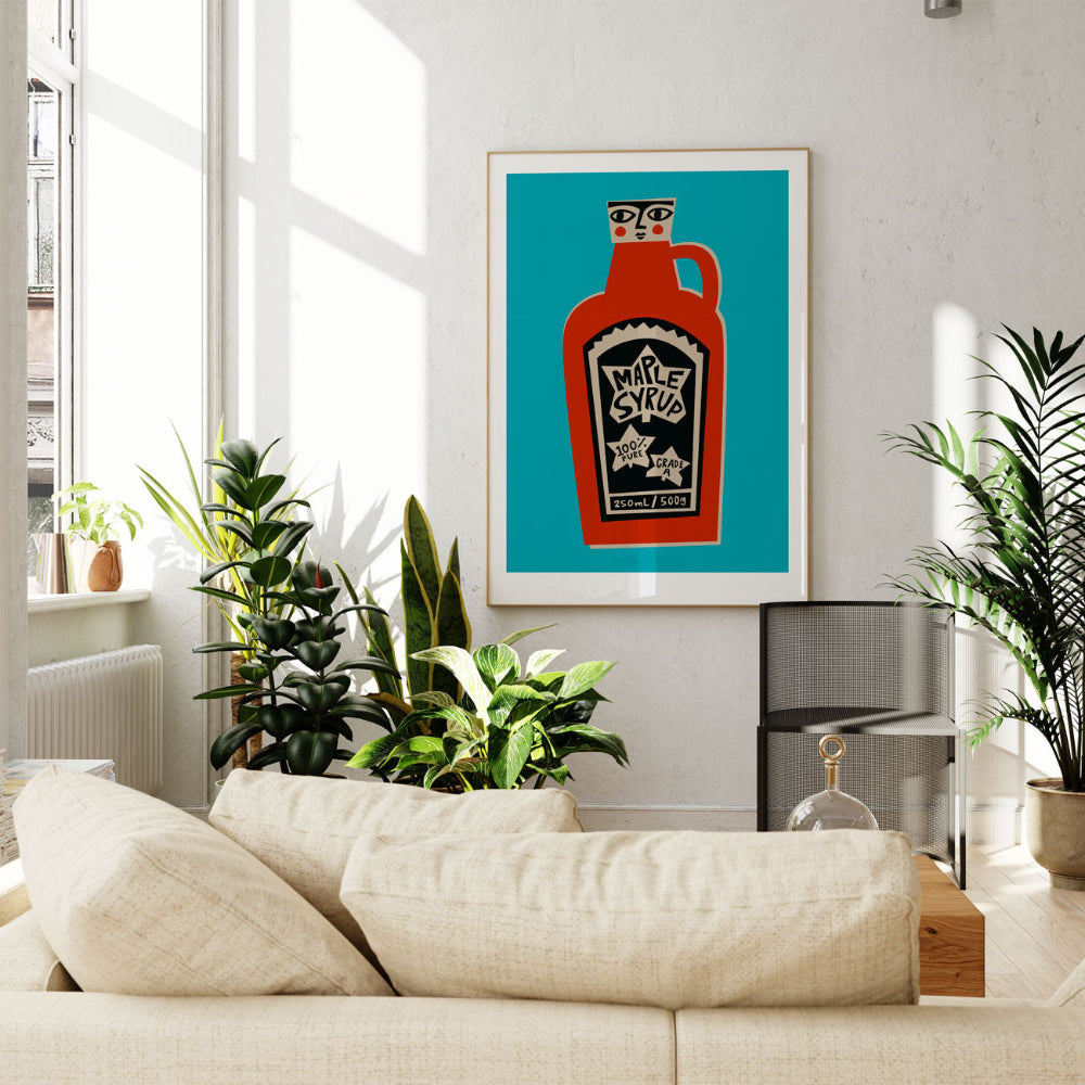 Maple Syrup print framed above a cream sofa in a bright living room with leafy indoor plants.