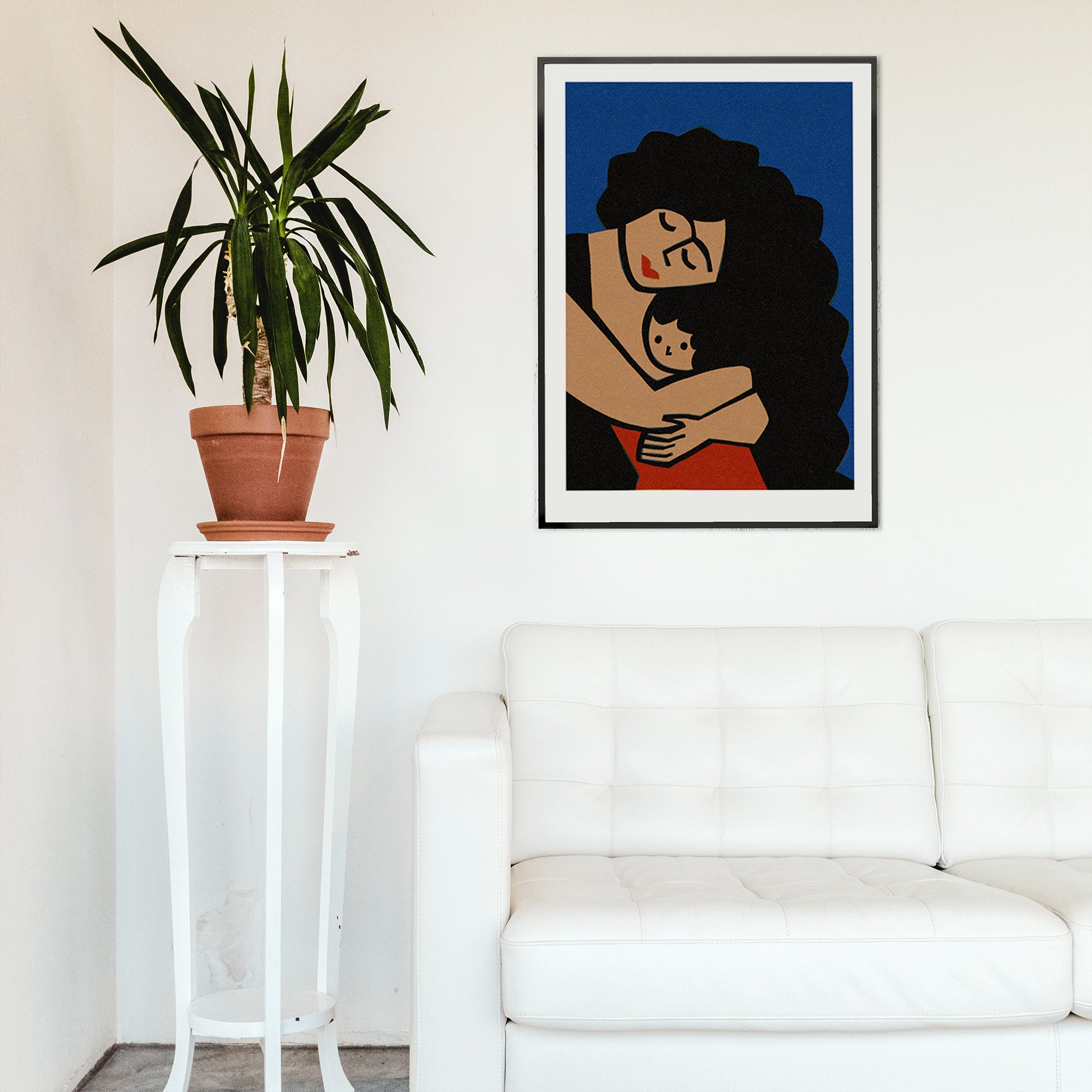 Framed mother and child illustration displayed on a white wall above a minimalist couch, the dark navy background making the intimate composition stand out.

