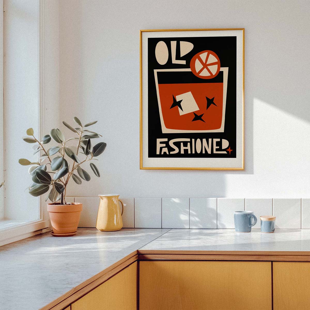 A framed vintage-style poster with the words 'OLD FASHIONED' hangs on a light wall above a kitchen counter. The poster features a bold retro drink illustration in orange, black, cream, and red tones, surrounded by a gold frame.