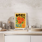 Orange-themed art print propped on a clean white benchtop in a modern home.