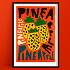 Pineapple art print featuring two graphic pineapples surrounded by overlapping “PINEAPPLE” text in bold, varied lettering, framed on a vivid orange wall.