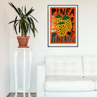 Pineapple print hanging above a white sofa and tall plant, bringing vibrant energy to a minimalist living space.