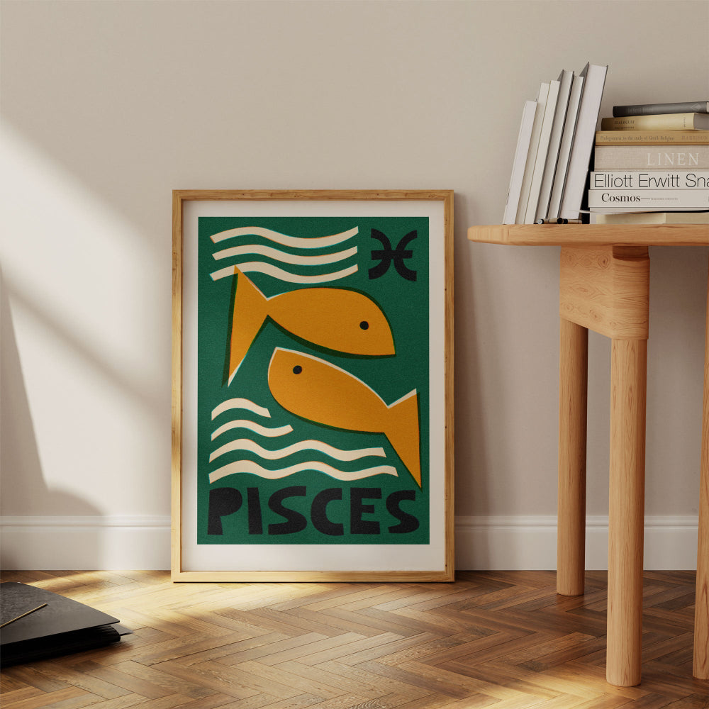 Pisces print framed on the floor beside a stack of books and wooden desk in a calm modern space.