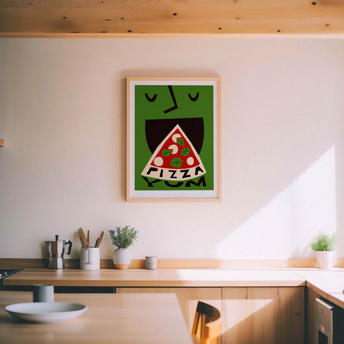 A framed art print featuring a stylized green face eating a slice of pizza with the word 'PIZZA' inside, hanging on a light beige wall above a wooden kitchen counter.