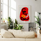 Abstract art print in red tones framed above cream sofa, styled with houseplants and soft light