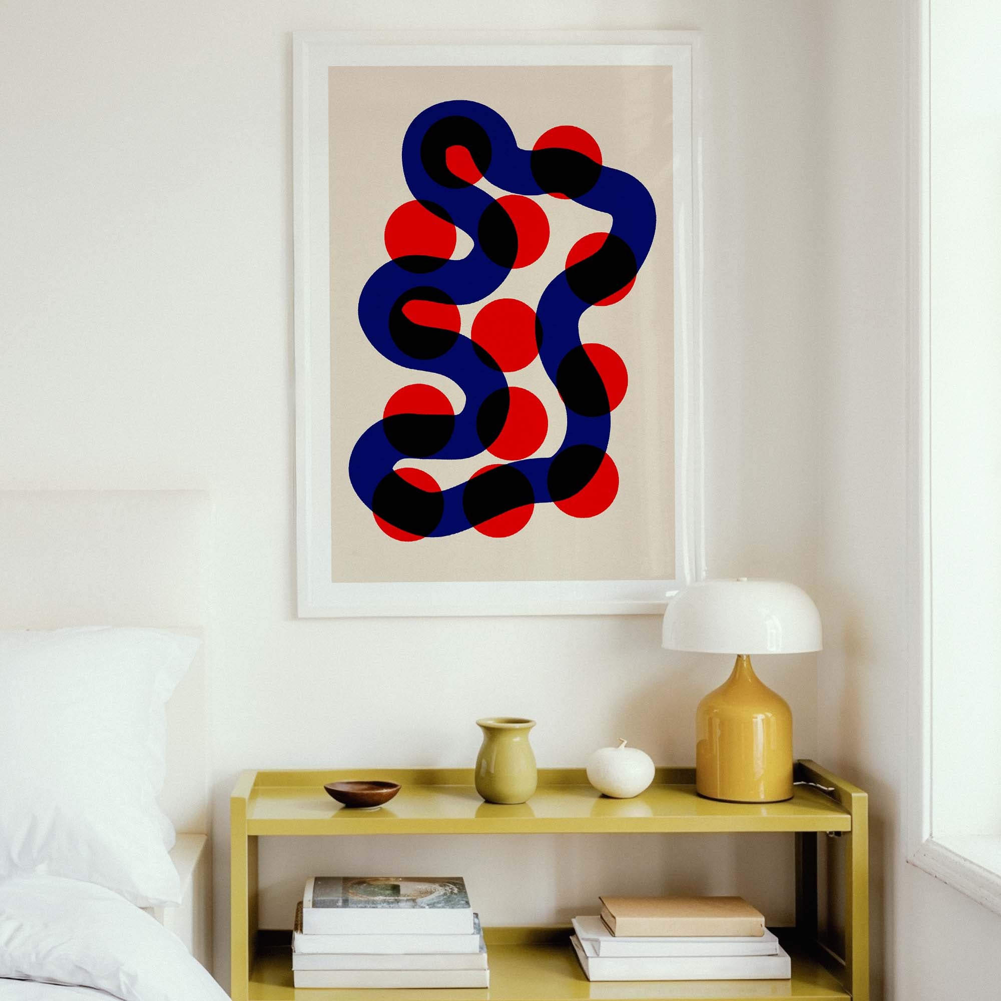 Abstract art print with blue and red circles on a beige wall above a shelf with decor items.