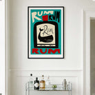 A framed vintage-style Rum poster hangs on a white wall above a glass bar cart with bottles and glasses. The poster features bold retro typography and a stylized bottle illustration in teal, cream, black, and red.
