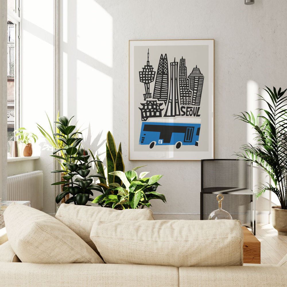 Seoul city print framed above a cream sofa surrounded by indoor greenery in a bright, modern space.
