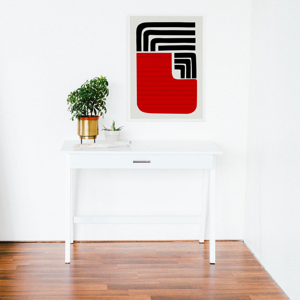 The Sol print hung above a minimal white desk in a bright room, its strong lines and red tone creating a grounded yet energetic presence.
