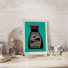 Soy Sauce print framed on a stone-textured kitchen shelf with small plates and cocktail glasses.