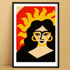 Sun Goddess art print in black frame, bold retro portrait with sunburst hair and warm tones.