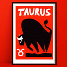 Taurus zodiac art print featuring a bold black bull illustration with white horns and the Taurus symbol, framed on deep red wall.
