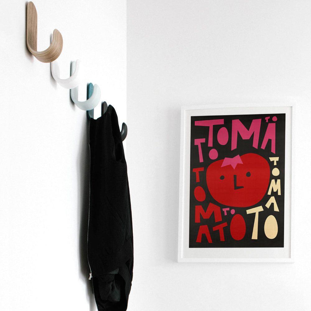 Wall art of a tomato character near coat hooks, styled in a modern hallway.