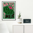 Watermelon poster framed above a white console with a speaker and potted plant, adding bold colour to a clean minimalist room.