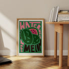 Watermelon print resting on the floor beside a wooden desk, styled in a light, relaxed corner of a modern home.