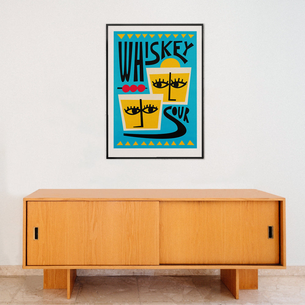 Whiskey Sour poster framed above light wood sideboard in a clean, modern interior space