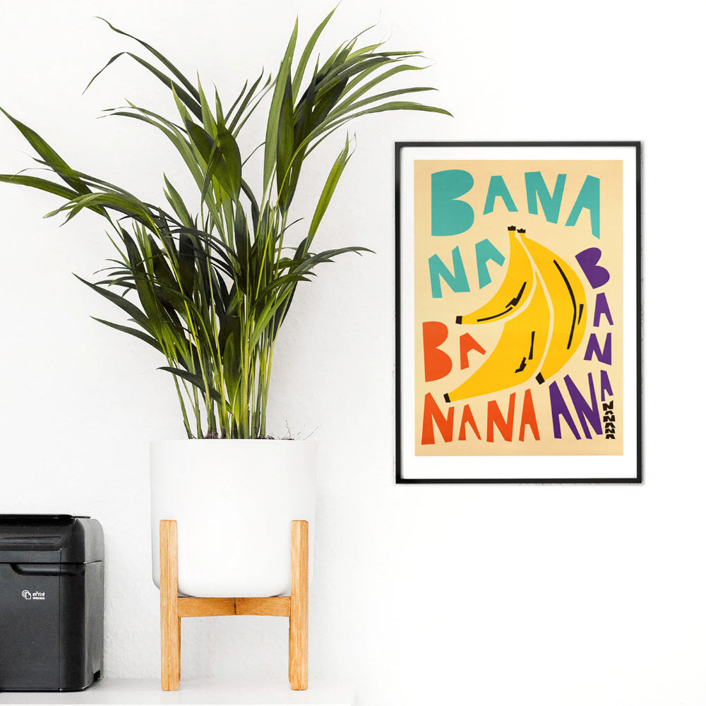 A vivid banana-themed art print styled in a bright room with houseplants and light wooden accents.