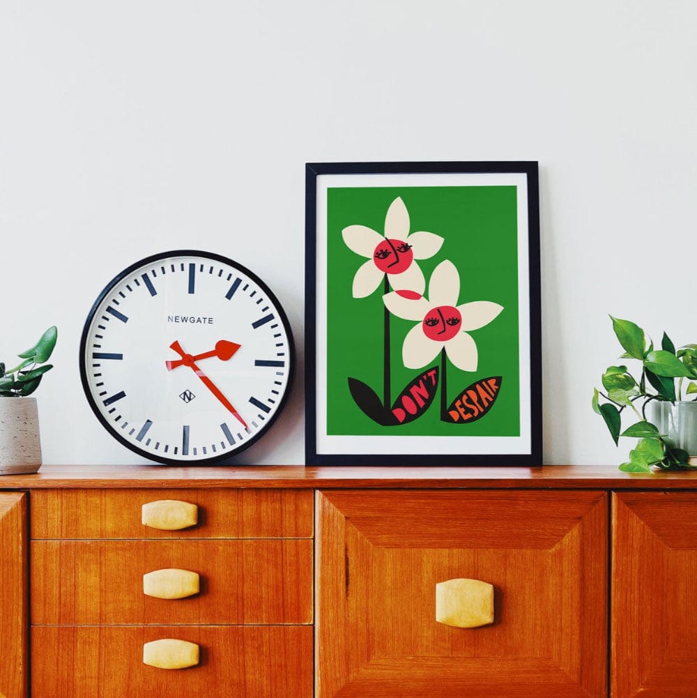Don’t Despair print framed above a vintage wooden cabinet, styled with plant and clock.