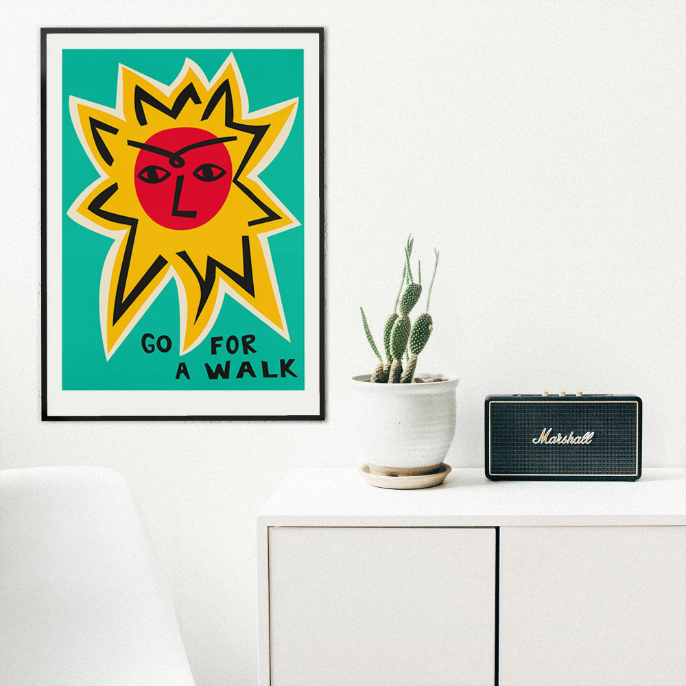Motivational sun print framed in a minimalist white room beside a speaker and small plant.