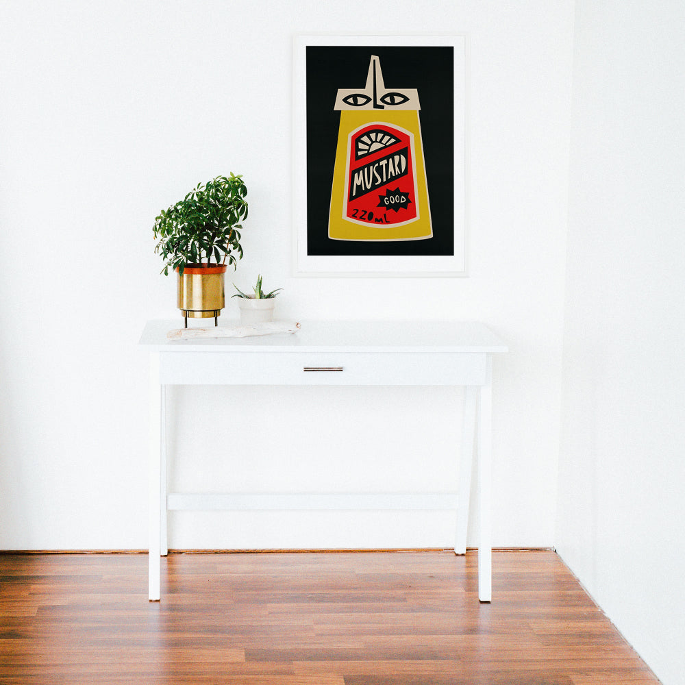 Mustard print framed above a clean white desk with minimal decor and wooden flooring.
