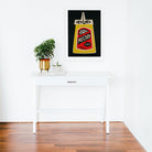 Mustard print framed above a clean white desk with minimal decor and wooden flooring.

