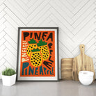 Pineapple poster propped up in a white herringbone kitchen nook with cutting boards and natural textures.