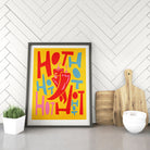 Framed chilli-themed artwork resting against a herringbone kitchen wall.